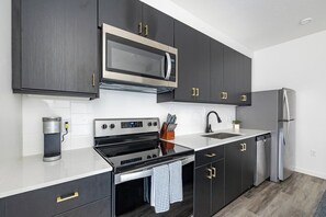 A modern kitchen with dark cabinetry, stainless steel appliances, and a white countertop. - Landing | Beautiful Studio in Central City (Salt Lake City)