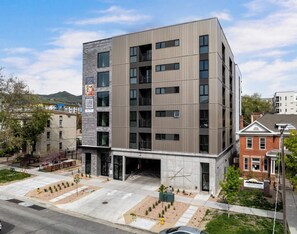 A multi-story building with a modern design, featuring a mix of glass and metal facade, and a ground-level entrance with a landscaped area. - Landing | Stunning Studio in Central City (Salt Lake City)