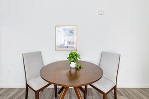 A round wooden table with two grey upholstered chairs, a potted plant, and a framed picture on the wall. - Landing | Beautiful Studio in Central City (Salt Lake City)