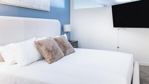 A neatly made bed with white and beige pillows, a bedside table with a lamp, and a TV mounted on the wall. - Landing | Spectacular 1BD in Central City (Salt Lake City)
