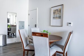 Un área de comedor con una mesa redonda, cuatro sillas grises tapizadas, una silla de madera y un cuadro enmarcado en la pared.