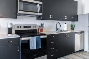 Una cocina moderna con muebles oscuros, microondas integrado, estufa de acero inoxidable y lavavajillas.