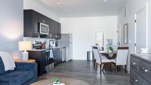 A modern kitchen with dark cabinets, stainless steel appliances, and a dining area with a wooden table and chairs. - Landing | Modern 1BD in Central City (Salt Lake City)