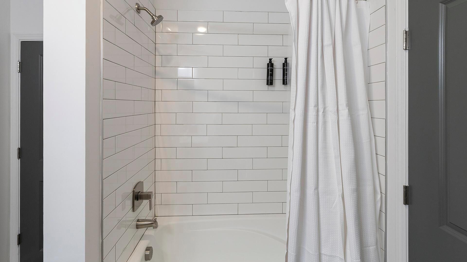 A modern bathroom with white subway tiles, a shower with a handheld showerhead, and a white shower curtain.