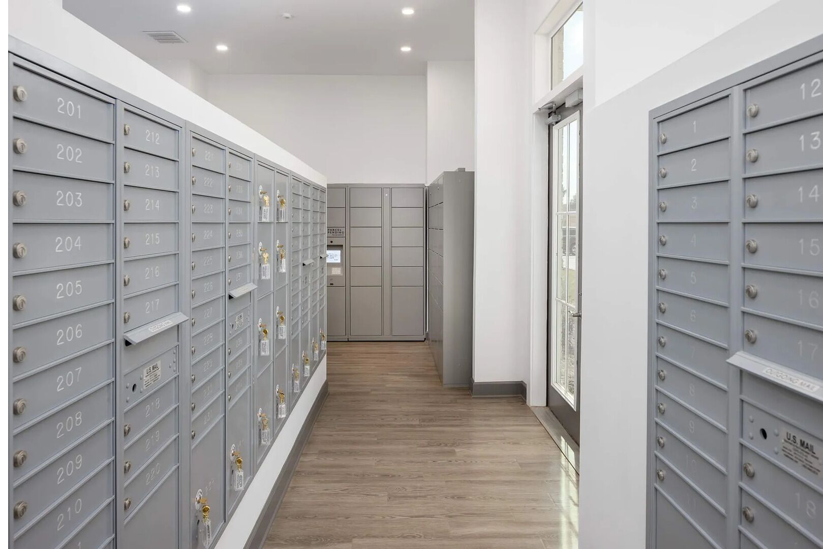 A row of grey mailboxes with numbers, a wooden floor, and a door at the end.