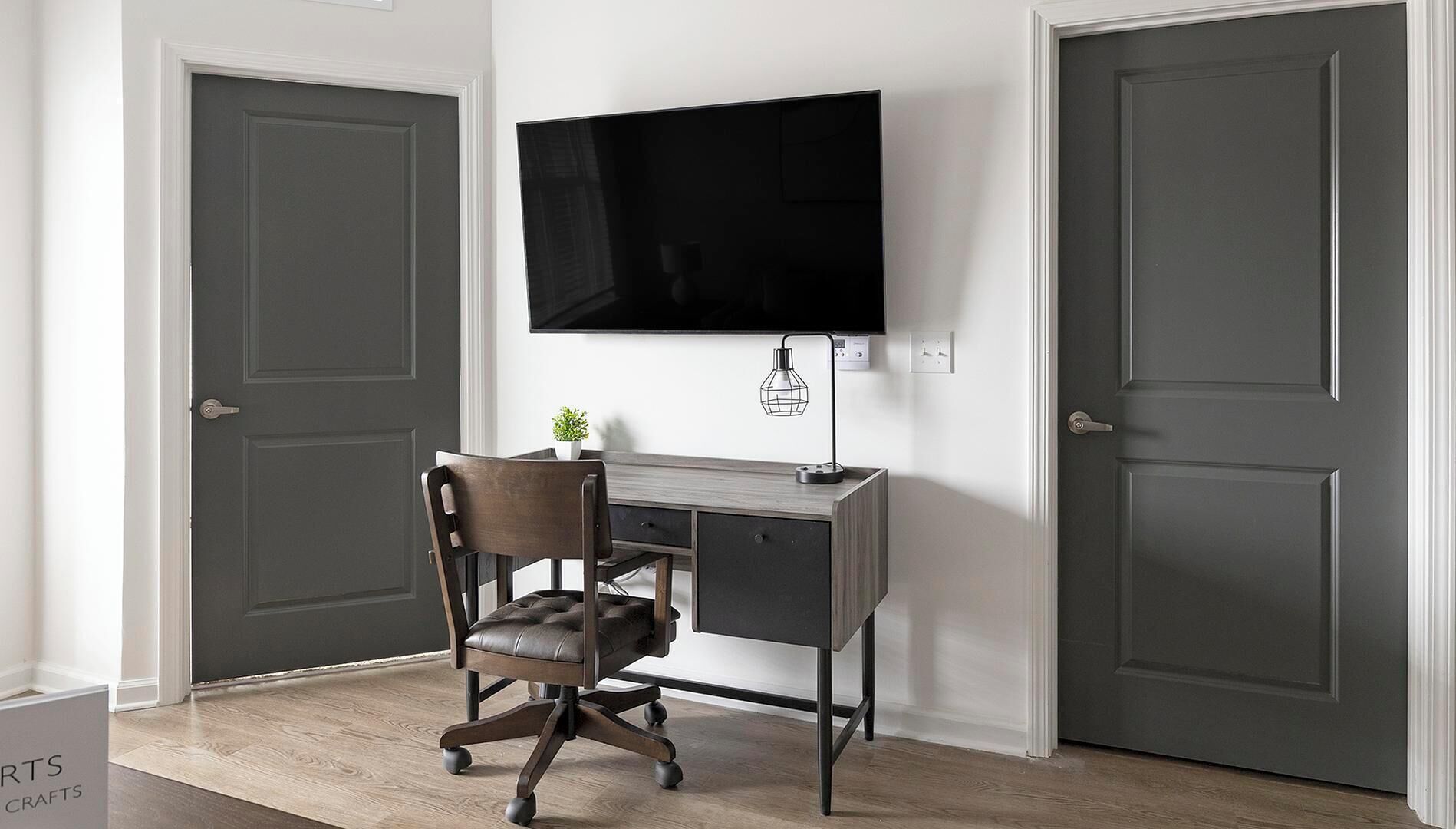 Un pequeño espacio de oficina con un escritorio, una silla y un televisor de pantalla plana montado en la pared.
