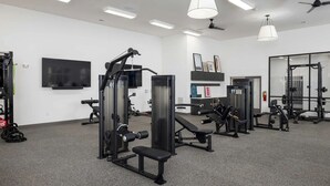 A gym with various exercise equipment, a flat-screen TV, and ceiling fans.