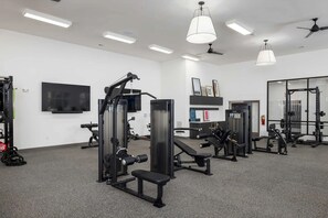 A gym with various exercise equipment, a flat-screen TV, and ceiling fans.