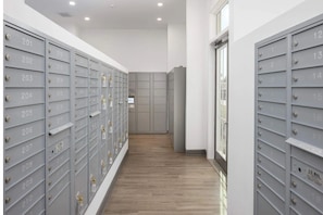 A row of grey mailboxes with numbers, a wooden floor, and a door at the end.