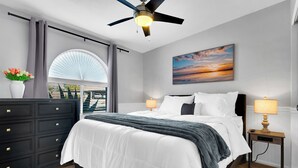 Een moderne slaapkamer met een bed, nachtkastjes, een dressoir, een plafondventilator en een groot raam met uitzicht.