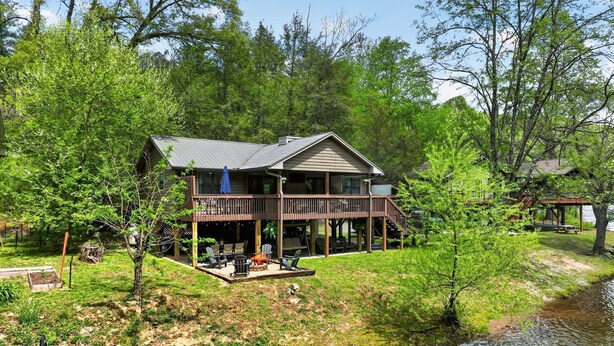 A two-story cabin with a deck, surrounded by trees and a body of water.