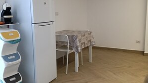 Eine kleine Küche mit einem weißen Kühlschrank, einer Kaffeemaschine und einem Tisch mit gemustertem Tischläufer.