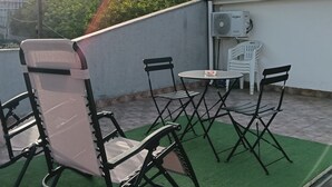 Eine Dachterrasse mit Tisch und Stühlen, einer Klimaanlage und Blick auf ferne Berge.
