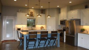 A modern kitchen with white cabinets, a central island with bar stools, stainless steel appliances, and pendant lighting. - POC 4 Bedroom, 3 bath Barndominium close to Froggies and 5D (Port Lavaca)
