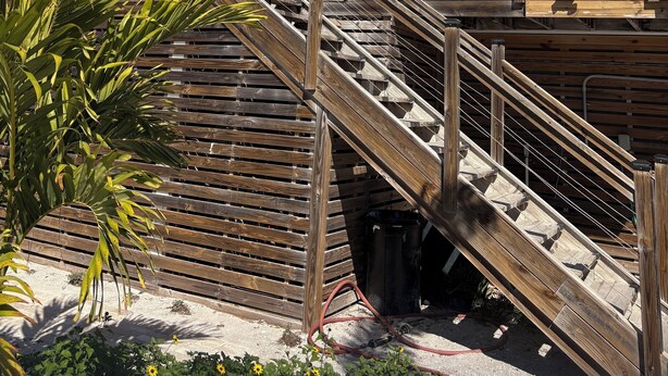 Ein zweistöckiges Gebäude mit einer Holztreppe, die zum Eingang führt, umgeben von Pflanzen und einem Holzzaun.