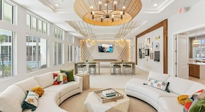 A spacious hotel lobby with a large chandelier, a TV mounted on the wall, and a dining area with a bar. - Landing | Amazing 1BD, Gym, Clubhouse (Palm Bay)
