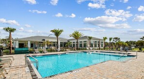 A swimming pool with a brick deck, lounge chairs, palm trees, and a building with a grey roof. - Landing | Chic 1BD, Clubhouse, Game Room (Palm Bay)