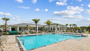 A swimming pool with a brick deck, lounge chairs, palm trees, and a building with a grey roof. - Landing | Stylish 2BD, Pool, Game Room (Palm Bay)