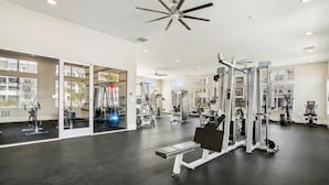 A spacious gym with various exercise equipment, large windows, and a ceiling fan. - Landing | Stylish 2BD, Pool, Game Room (Palm Bay)