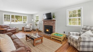 A living room with a fireplace, leather sofas, a coffee table, and plaid-patterned chairs. - Peaceful Lakes Region Retreat  | Canoe + Fire pit (Meredith)