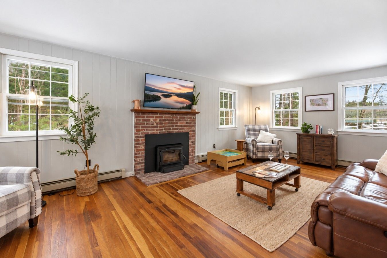 A living room with a fireplace, a television, a sofa, a coffee table, and a view of the outdoors through large windows.