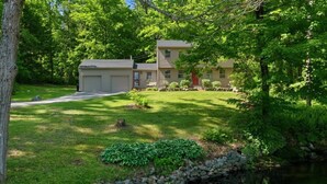A two-story house with a well-maintained lawn, a stone wall, and a small pond. - Peaceful Lakes Region Retreat  | Canoe + Fire pit (Meredith)