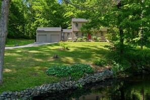 Ein zweistöckiges Haus mit gepflegtem Rasen, einer Steinmauer und einem kleinen Teich.