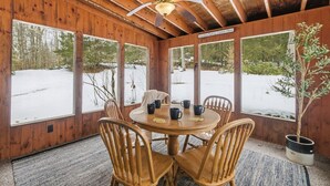 A wooden cabin with a round table and chairs, large windows, and a ceiling fan. - Peaceful Lakes Region Retreat  | Canoe + Fire pit (Meredith)
