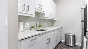 Una cocina moderna con armarios blancos, un lavamanos de acero inoxidable y un cubo de basura.