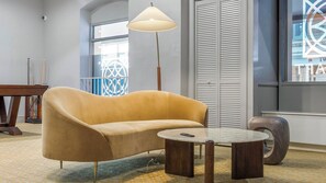 A room with a sofa, a lamp, a table, and a window with blinds. - Landing | Incredible 1BD, Gym (New Haven)
