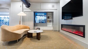 A modern living room with a sofa, a small round table, a fireplace, and a large window with a decorative view. - Landing | Incredible 1BD, Gym (New Haven)