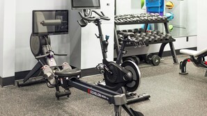 Ein Fitnessstudio mit Trainingsgeräten, darunter ein Rudergerät, Kurzhanteln und eine Trainingsbank.