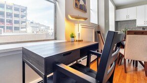 Une cuisine moderne avec des meubles blancs, un plan de travail noir et une vue sur le paysage urbain, visible à travers une grande fenêtre.