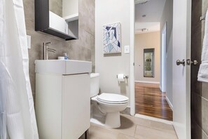 A modern bathroom with a white sink, toilet, and shower area. - Landing | Incredible 1BD, Gym (New Haven)