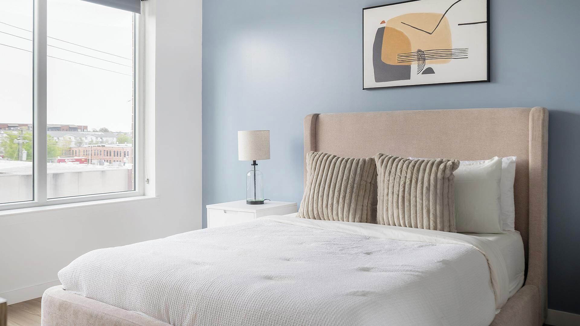 A neatly arranged bedroom with a bed, a bedside table with a lamp, and a framed picture on the wall.