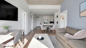 Un soggiorno moderno con zona pranzo, un divano, una TV e una cucina sullo sfondo.
