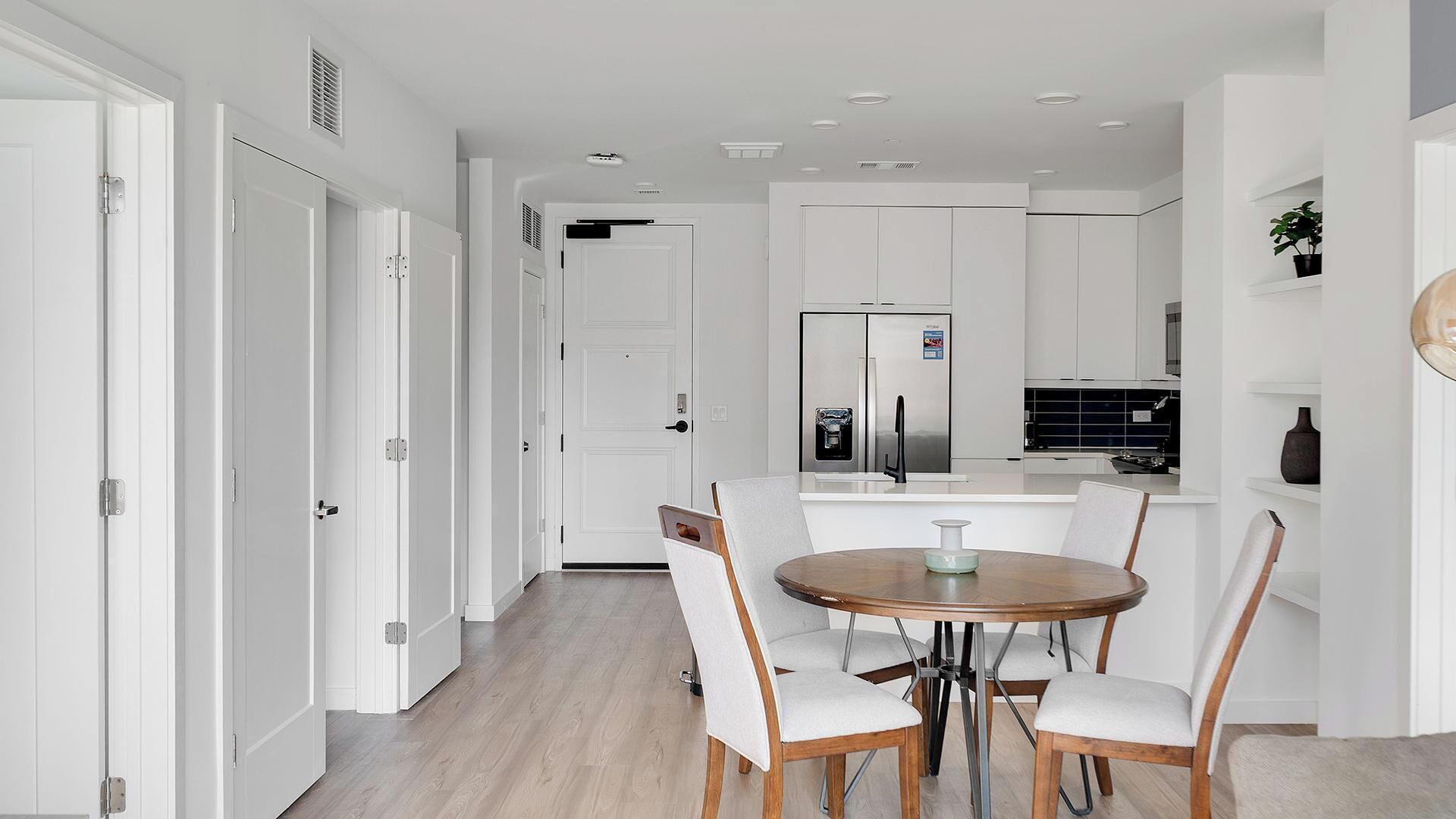 Une cuisine moderne avec des meubles blancs, un réfrigérateur en acier inoxydable et un coin repas comprenant une table ronde et des chaises.
