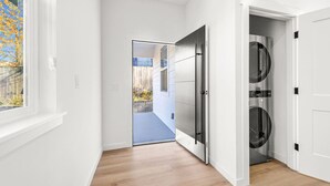 A hallway with a wooden floor, white walls, and a door leading to a laundry area with two dryers. - Modern Comfort in Seattle, 10 mins to downtown (Seattle)
