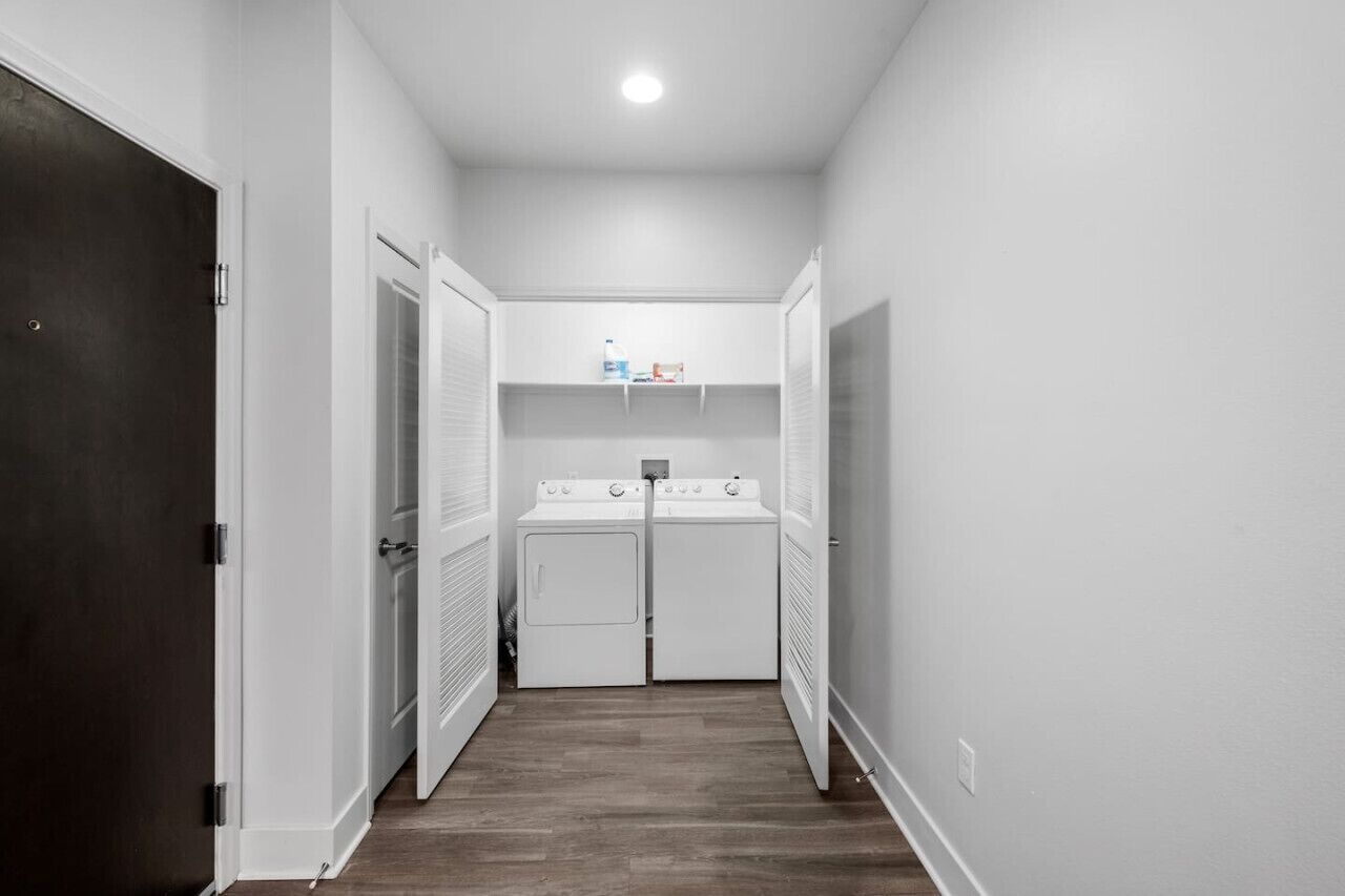 A laundry room with two white dryers and a shelf above them.