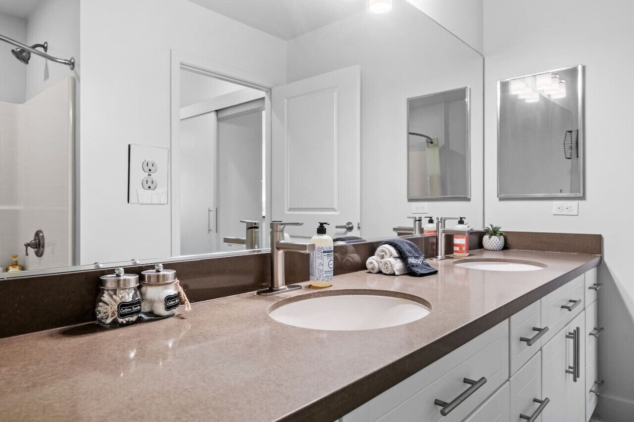 Une salle de bain moderne avec deux lavabos, un grand miroir et un porte-serviettes.