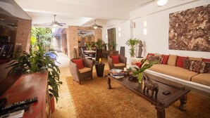 A spacious living area with a sofa, armchairs, and a coffee table. There are ceiling fans, a large abstract painting, and a variety of plants. - Best location; magical 4BR house w/ large pool (Cartagena de Indias)