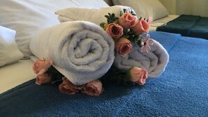 A neatly made bed with rolled towels and a bouquet of roses. - Condominio Summer Park Bloco i (Brasília)