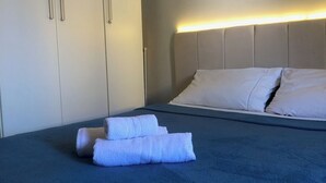 A neatly made bed with a blue cover, white pillows, and folded towels on the bed. - Condominio Summer Park Bloco i (Brasília)