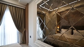 A modern hotel room with a large bed, a window with a geometric metal frame, and a view of the outdoors.