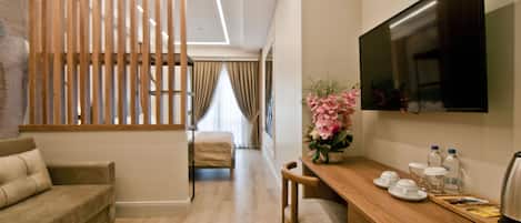 A modern hotel room with a wooden partition, a sofa, a dining table with a TV, and a vase of flowers.