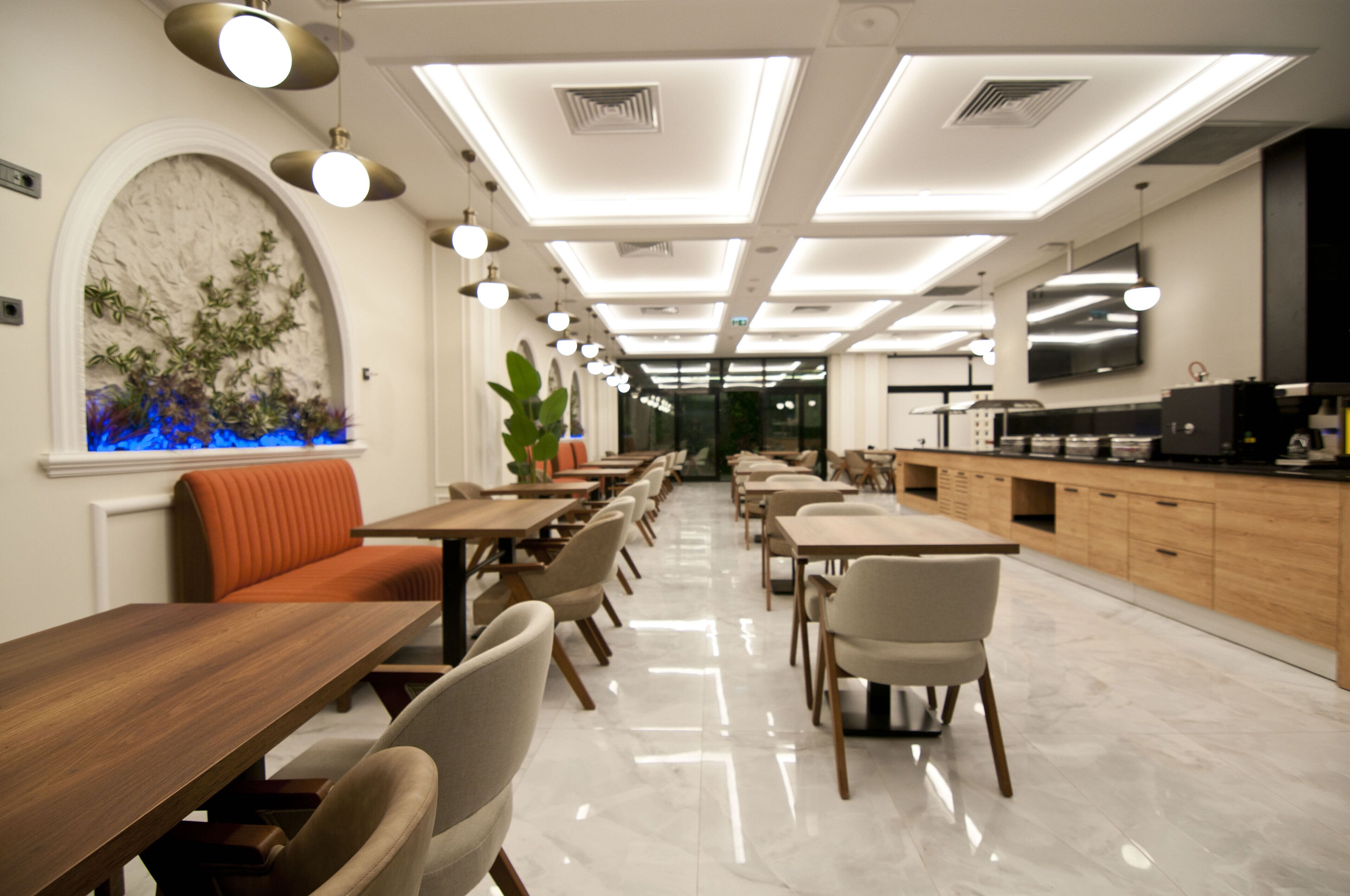 A modern restaurant with a long counter, multiple tables, and a seating area with a sofa.