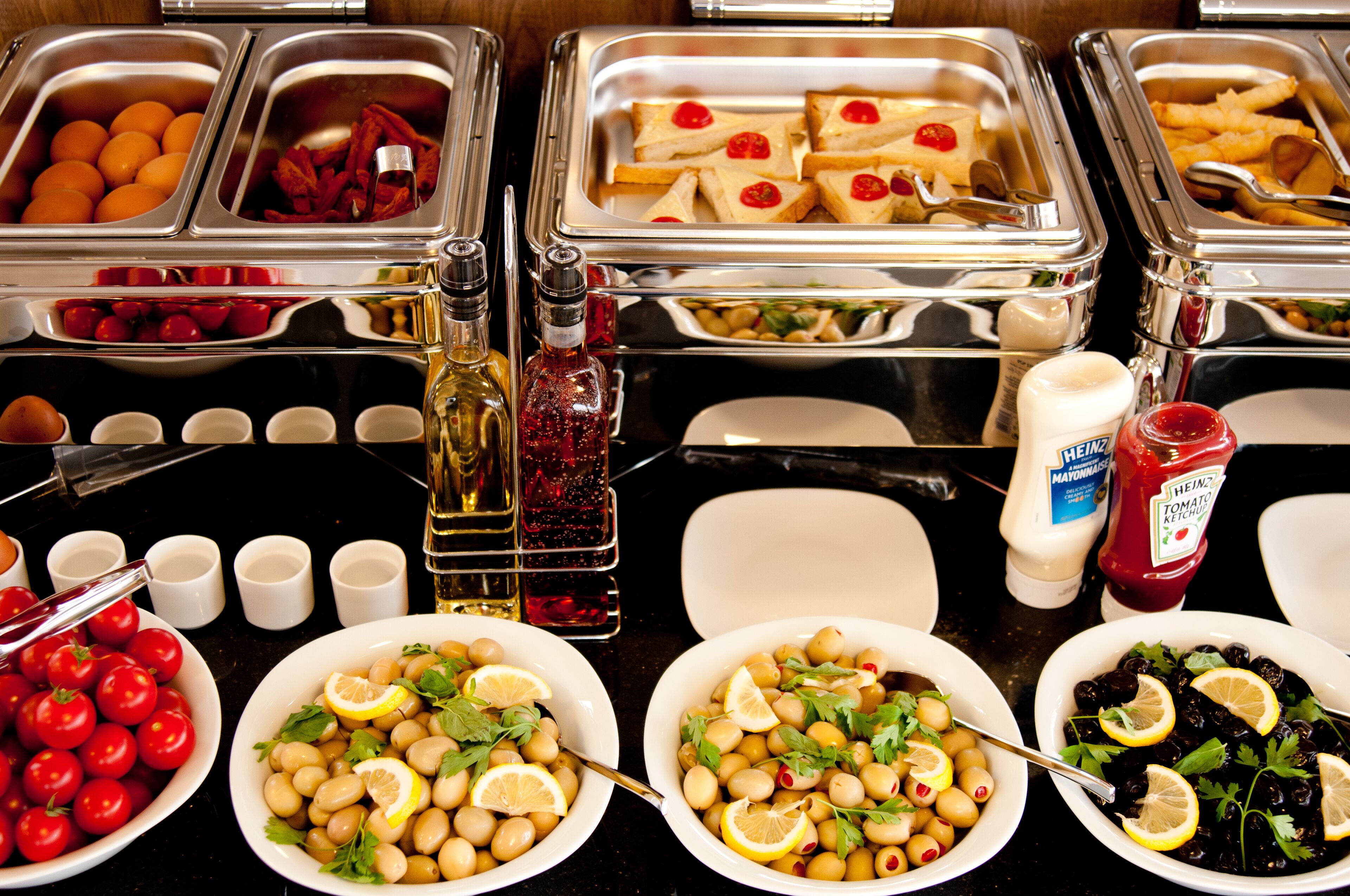 Buffet com diversas opções de comida, incluindo azeitonas, tomates e pão.