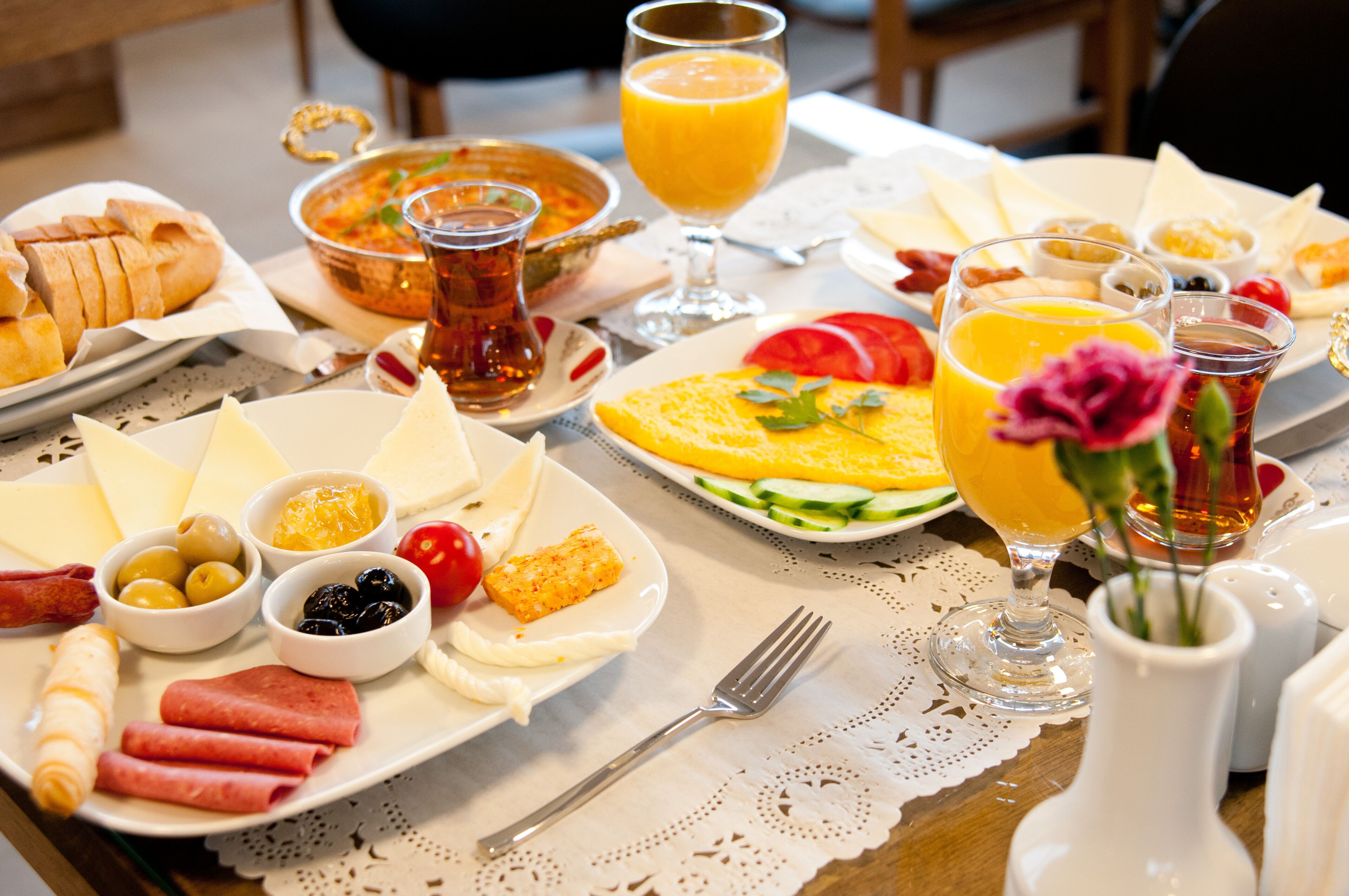 A breakfast table with various dishes, including bread, cheese, olives, and a fruit salad.