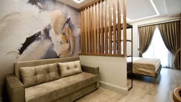 Quarto moderno com sofá bege, divisória de ripas de madeira, cama com cobertura bege e uma grande pintura abstrata na parede.