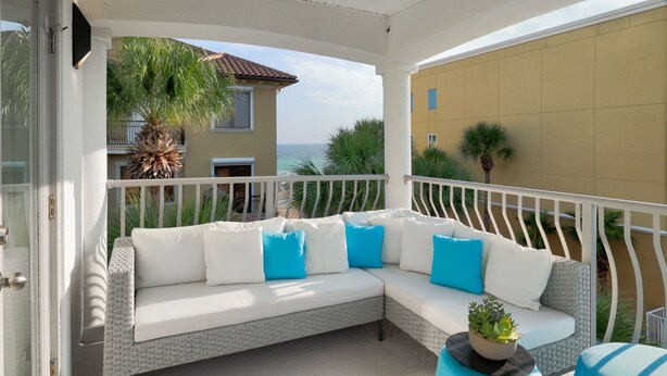 A covered balcony with a white sofa, blue cushions, and a potted plant. - H2O Living•Pool & Hot Tub•Game Room•Private Beach •Free Chair Service+Beach Gear (Miramar Beach)